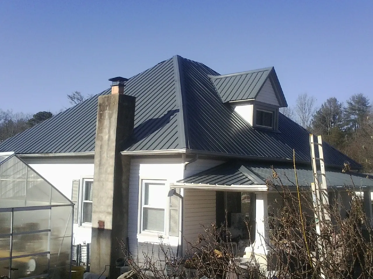 Dark blue standing seam metal roof on a white farmhouse with dormer — Slate & Tile Roof Repair by Roofing Brothers in Three Forks
