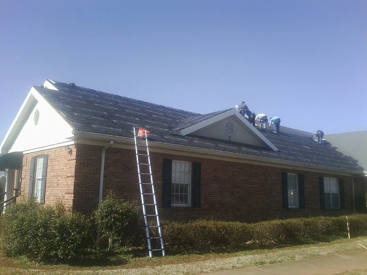 Crew tearing shingles off a brick ranch roof with a ladder set — Emergency Roof Repair work by our crew in Three Forks