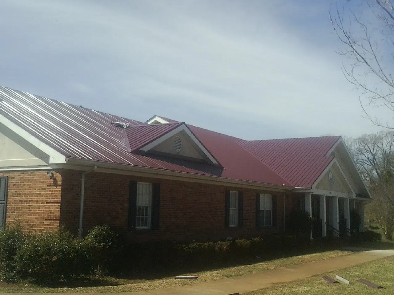 Red metal roof with gabled entries on a long brick building, from a Hail Damage Roof Repair job in Three Forks