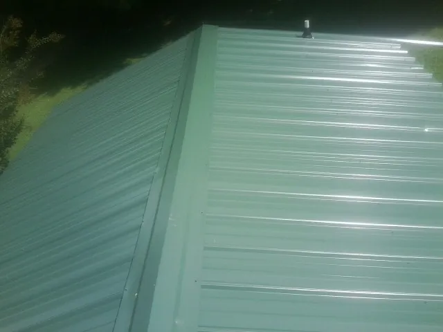 New green metal panels meeting at the ridge of a roof — Flat Roof Repair work by our crew in Three Forks