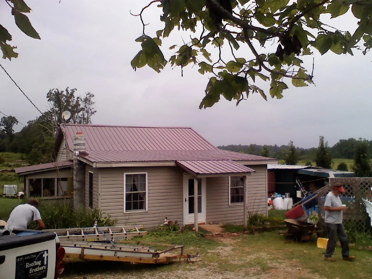 Crew finishing a mauve metal roof on a small farmhouse in Three Forks