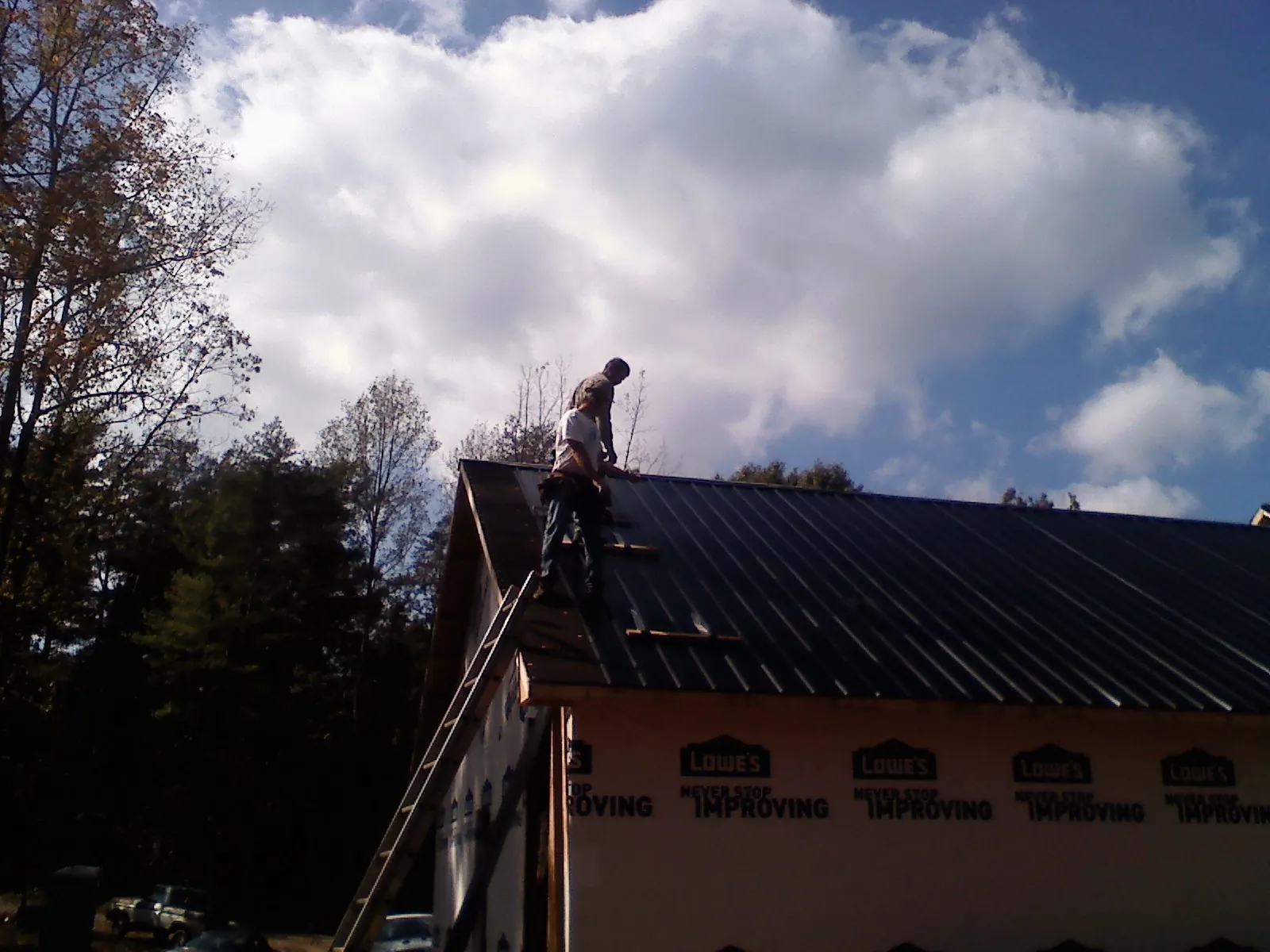 Roofer fastening dark metal panels high against a cloudy sky, from a Roof Inspection job in Three Forks