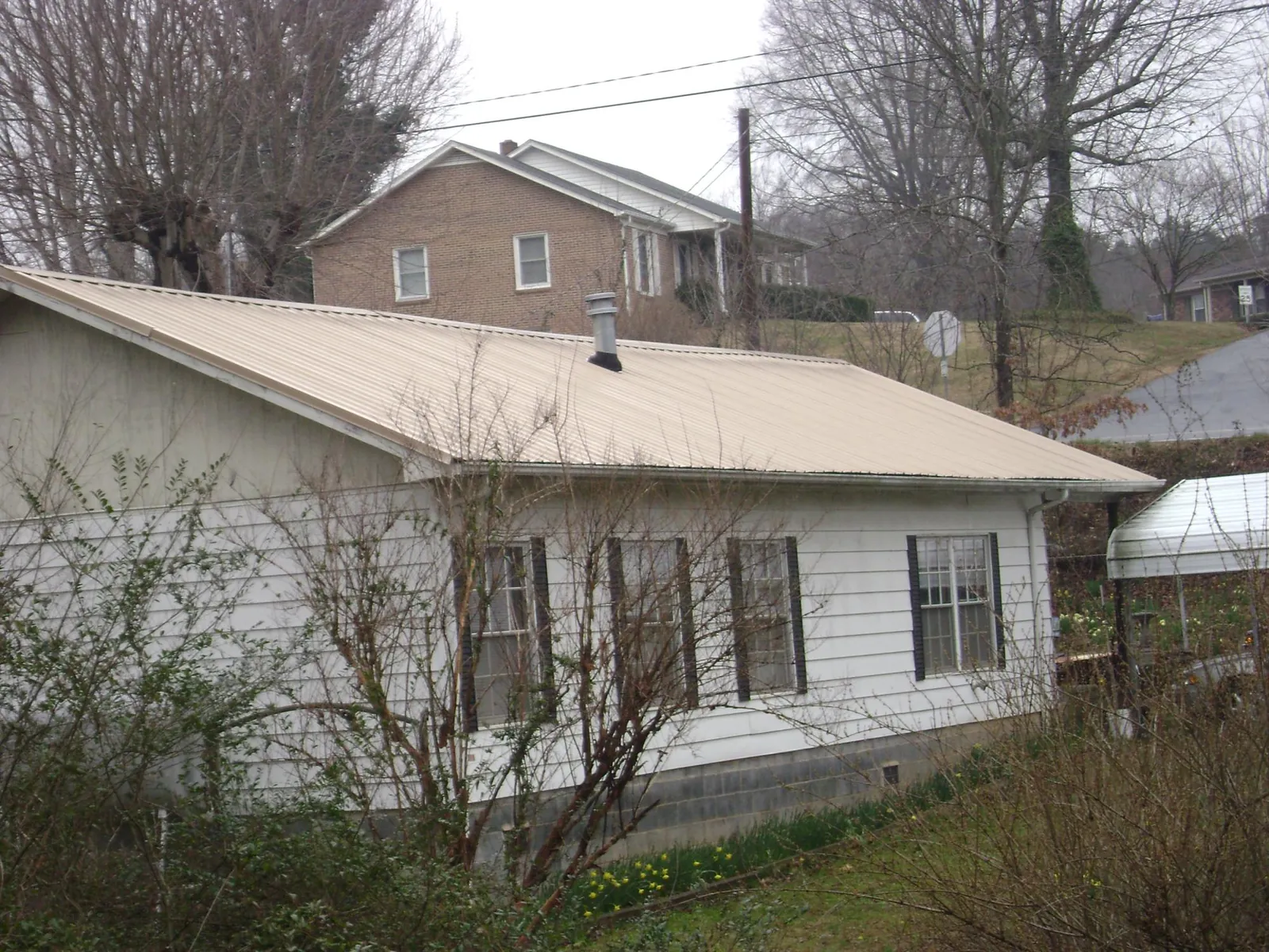 Tan metal roof on a white sided house set into a hillside — Commercial Roofing by Roofing Brothers in Three Forks