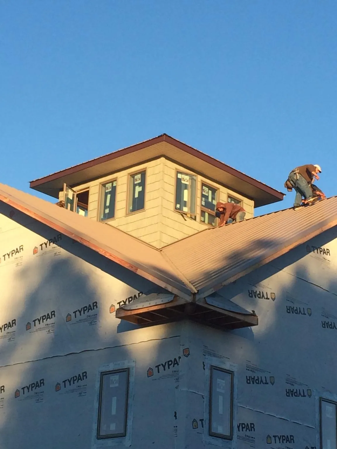 Roofers working around a rooftop cupola on a new metal roof at sunset — Roof Waterproofing in Three Forks by Roofing Brothers